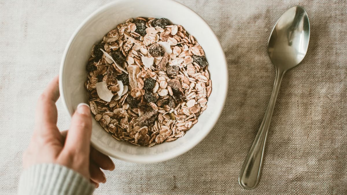 A close-up of a healthy muesli breakfast bowl with a hand and spoon on a table.